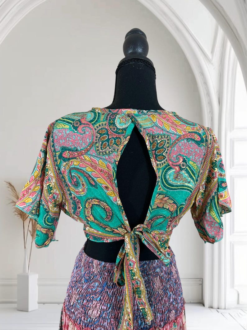 May include: A colorful paisley print top with a keyhole back and tie closure. The top features shades of teal, pink, yellow, and green. The bottom portion of the outfit is a multi-colored skirt with a ruffled design.
