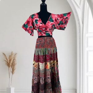 May include: A two-piece outfit on a mannequin. The top is a wrap-style crop top with a V-neck and short sleeves, featuring a pink floral pattern with green accents. The skirt is a tiered maxi skirt with a patchwork design in various colors.