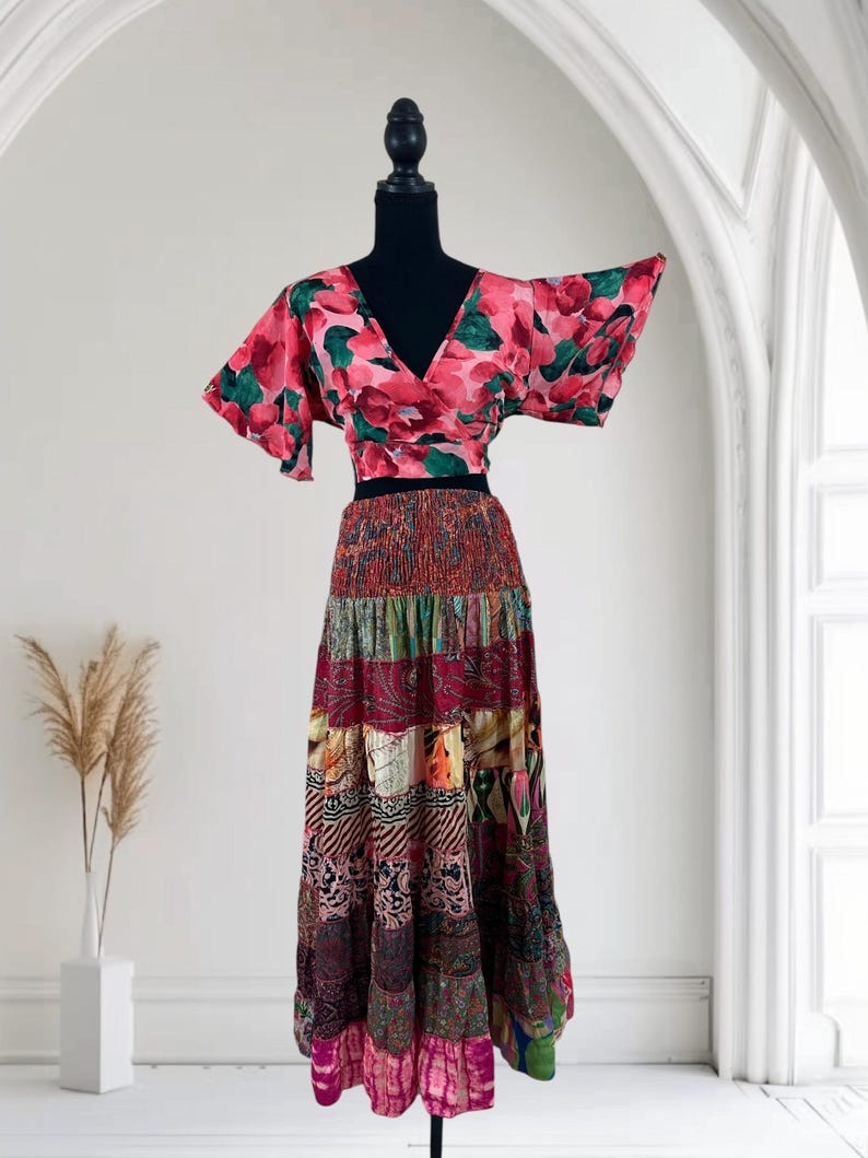 May include: A two-piece outfit on a mannequin. The top is a wrap-style crop top with a V-neck and short sleeves, featuring a pink floral pattern with green accents. The skirt is a tiered maxi skirt with a patchwork design in various colors.