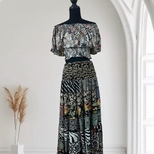 May include: A two-piece outfit on a mannequin. The top is an off-the-shoulder style with a floral pattern in muted colors. The skirt is a patchwork design with various patterns in black, white, and other colors. The outfit is displayed against a white background.