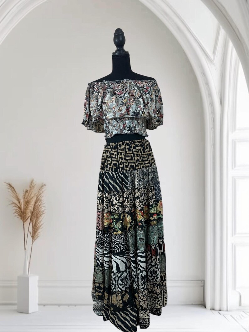 May include: A two-piece outfit on a mannequin. The top is an off-the-shoulder style with a floral pattern in muted colors. The skirt is a patchwork design with various patterns in black, white, and other colors. The outfit is displayed against a white background.