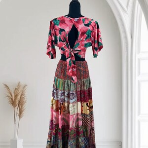 May include: A two-piece outfit on a mannequin. The top is a pink floral print with a keyhole back and tie closure. The skirt is a patchwork design in various colors and patterns, including pink, green, and brown.