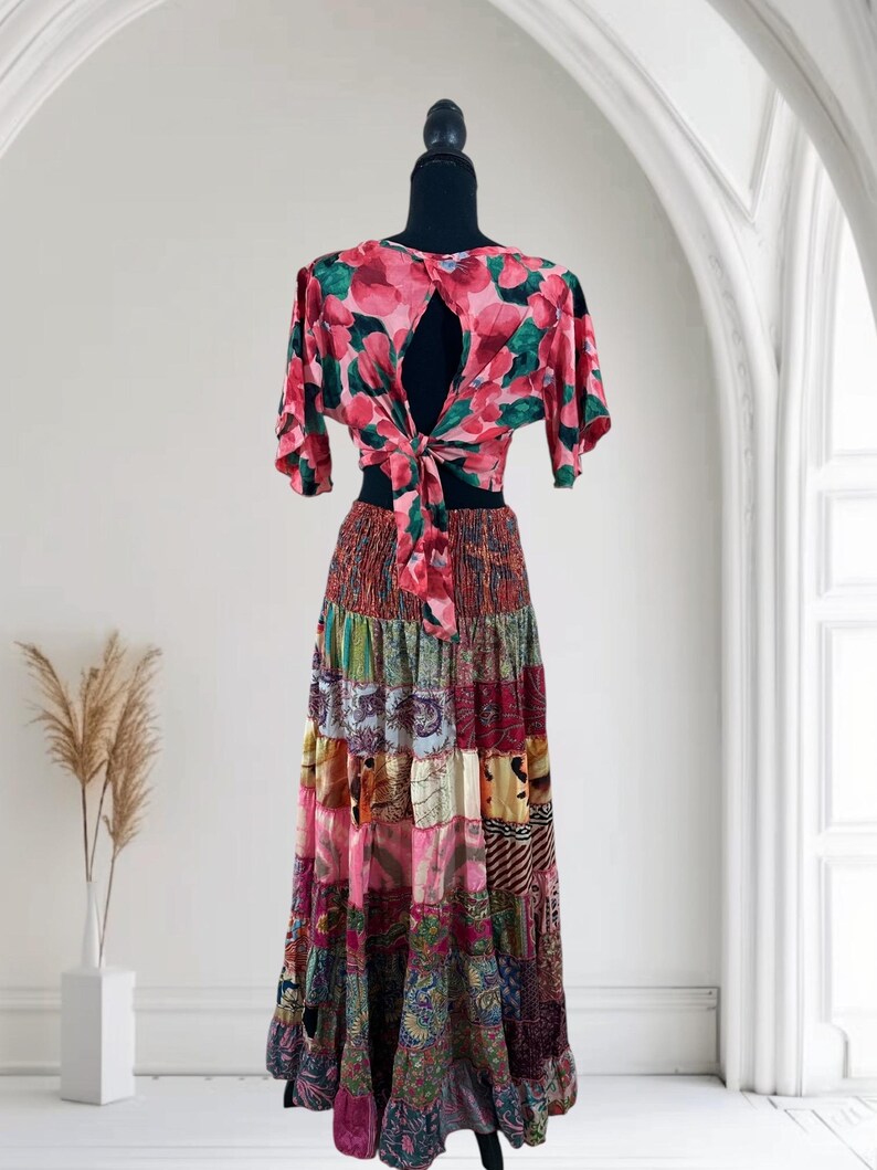 May include: A two-piece outfit on a mannequin. The top is a pink floral print with a keyhole back and tie closure. The skirt is a patchwork design in various colors and patterns, including pink, green, and brown.
