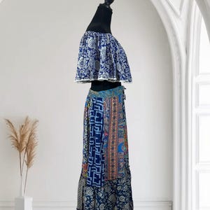 May include: A two-piece outfit on a mannequin. The top is a blue and white floral print off-the-shoulder crop top. The skirt is a patchwork design with various blue patterns and a drawstring waist. The outfit is displayed against a white background.