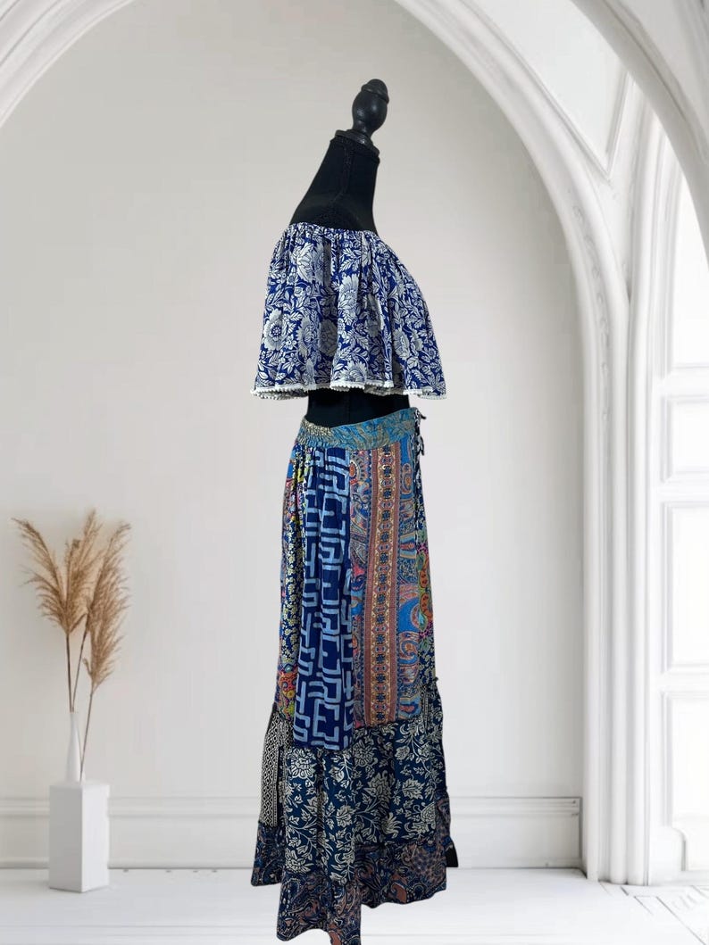 May include: A two-piece outfit on a mannequin. The top is a blue and white floral print off-the-shoulder crop top. The skirt is a patchwork design with various blue patterns and a drawstring waist. The outfit is displayed against a white background.