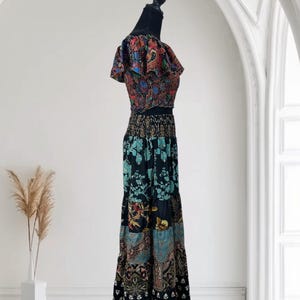 May include: A two-piece bohemian outfit on a mannequin. The top is a cropped style with ruffled sleeves, featuring a colorful paisley print. The long skirt has a tiered design with a patchwork of floral and geometric patterns in shades of black, blue, and red.