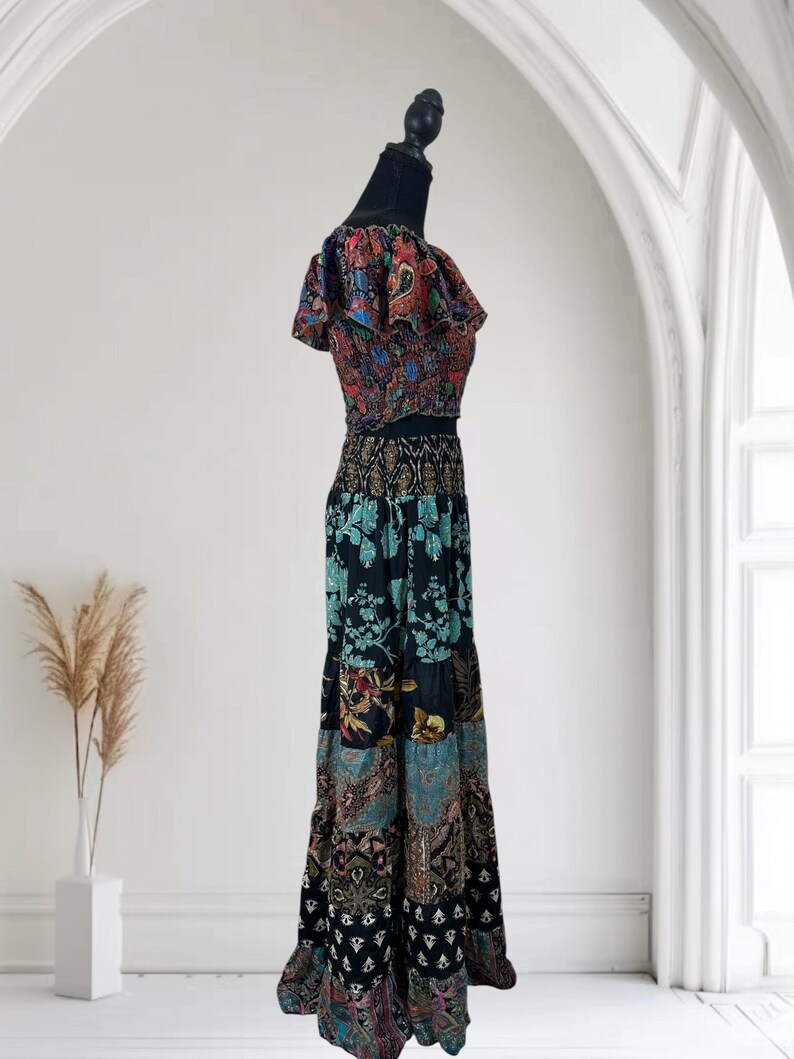 May include: A two-piece bohemian outfit on a mannequin. The top is a cropped style with ruffled sleeves, featuring a colorful paisley print. The long skirt has a tiered design with a patchwork of floral and geometric patterns in shades of black, blue, and red.