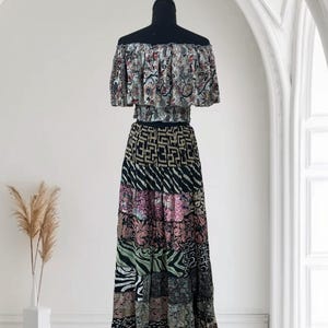 May include: A two-piece bohemian outfit on a black mannequin. The off-the-shoulder top features a floral pattern, while the long skirt showcases a patchwork design with various patterns and colors, including black, pink, and green.