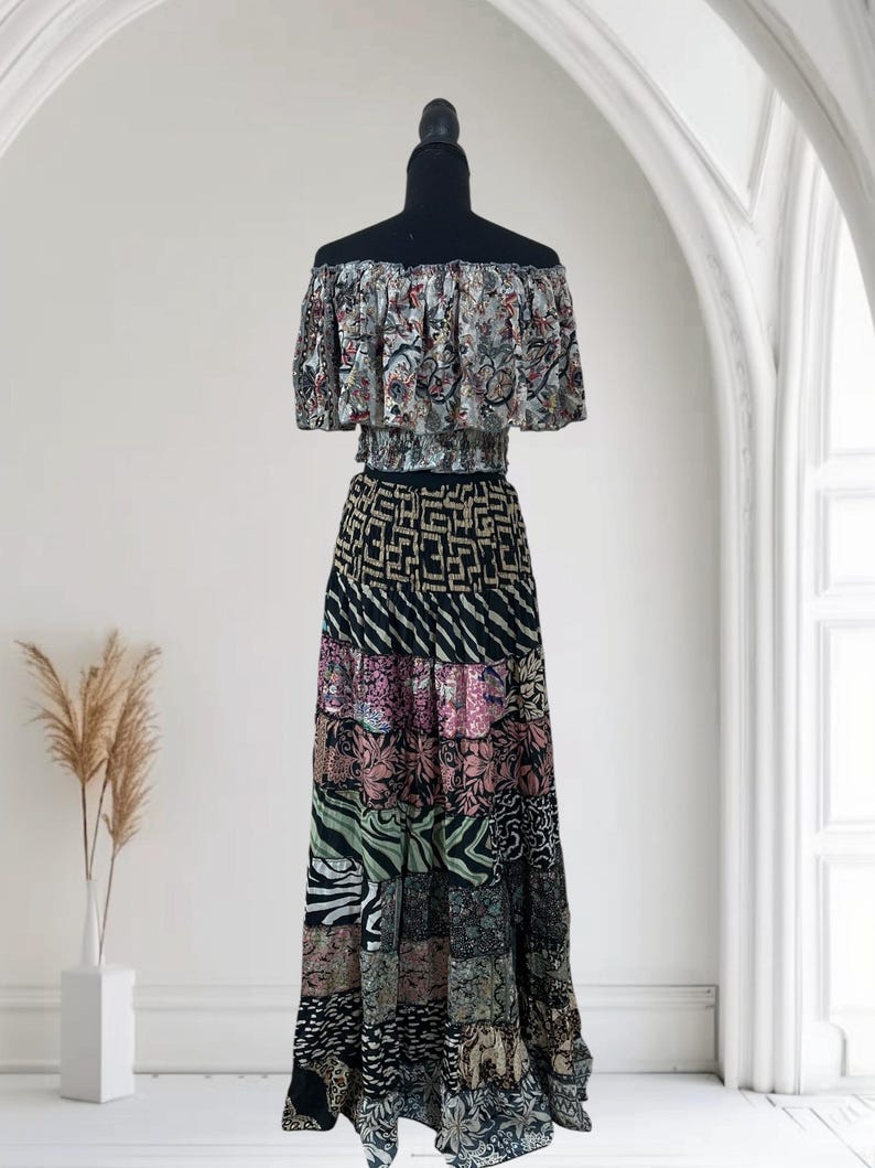 May include: A two-piece bohemian outfit on a black mannequin. The off-the-shoulder top features a floral pattern, while the long skirt showcases a patchwork design with various patterns and colors, including black, pink, and green.