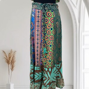 May include: A long, patchwork skirt with a variety of patterns and colors. The skirt features a mix of blue, green, brown, and patterned fabrics. It has a drawstring waist and a ruffled hemline. The skirt is displayed against a white background.