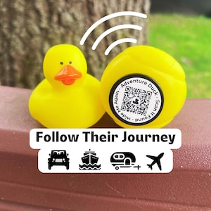 May include: Two yellow rubber ducks with orange beaks. One duck has a QR code sticker that says "Adventure Duck - Scan if found - Hide Me Again". The image also includes the text "Follow Their Journey" with travel icons.