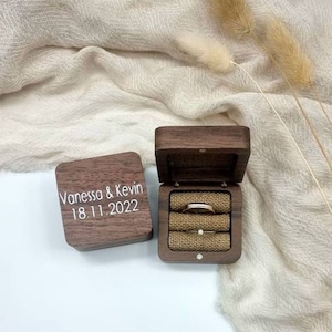 Pode incluir: Uma caixa de anel de madeira com uma tampa com dobradiças. A caixa é gravada com o texto "Vanessa & Kevin 18.11.2022". A caixa está aberta e um anel de ouro está dentro.