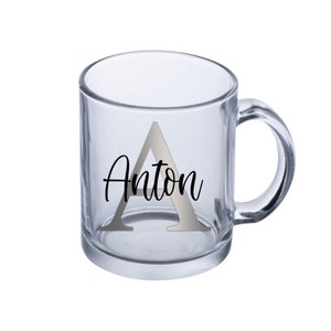 Puede incluir: Una taza de vidrio transparente con una letra A plateada y el nombre Anton impreso en negro.