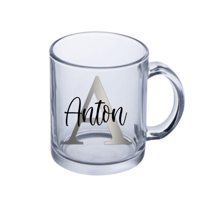 Puede incluir: Una taza de vidrio transparente con una letra A plateada y el nombre Anton impreso en negro.