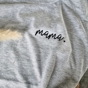 Op de afbeelding: Een grijs t-shirt met het woord "mama" in het zwart geborduurd op de voorkant.