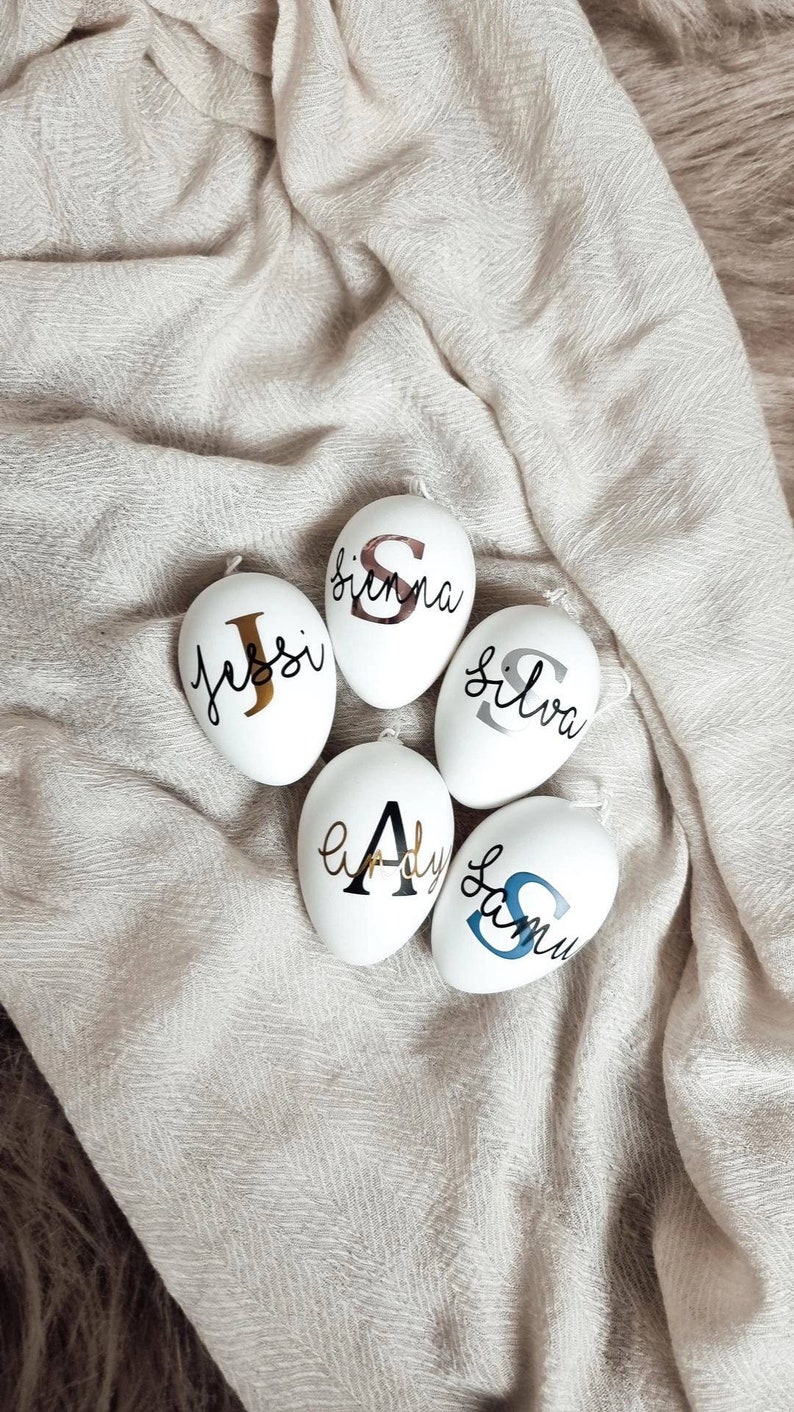 Op de afbeelding: Vijf witte eieren met verschillende namen erop geschreven in zwarte, gouden en blauwe letters. De namen zijn Jessi, Sienna, Silva, Lady en Samu.