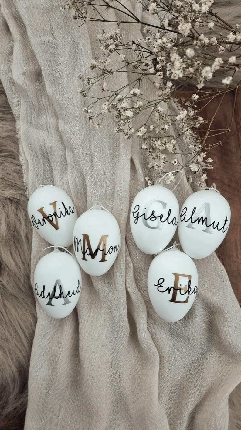 Op de afbeelding: Vijf witte paaseieren met gouden letters. De namen op de eieren zijn:  "Gisela", "Almut", "Marion", "Erika" en "Adelheid".