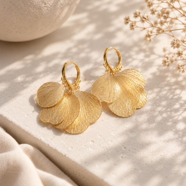 May include: A pair of gold-toned hoop earrings featuring multiple layered, fan-shaped metal charms. Each charm has a textured, linear surface finish that catches the light. The earrings are suspended from small circular hoops with a secure clasp mechanism.