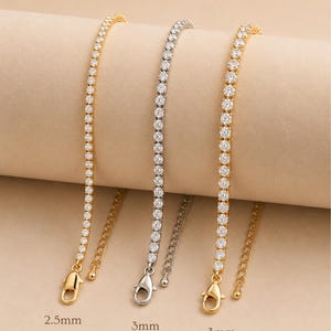 May include: Three tennis bracelets with clear, round-cut stones are displayed. One is gold-toned, labeled "2.5mm Delicate", and two are 3mm, one silver-toned "Classic" and one gold-toned "Gold". Each bracelet has a lobster clasp.