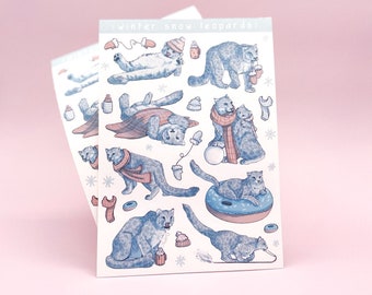 May include: A sheet of stickers featuring illustrations of snow leopards in various wintery scenes. The stickers are printed on white paper and feature a blue and pink color scheme. The text "winter snow leopards!" is printed at the top of the sheet.