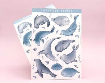 May include: A sheet of envelope seals featuring a variety of cute cartoon seals in different poses. The seals are drawn in shades of blue and gray, with some surrounded by small bubbles. The text "envelope seals" is printed at the top of the sheet.