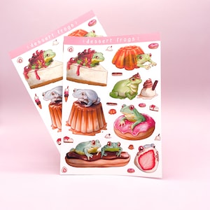 May include: Two sticker sheets featuring frog illustrations on desserts. The stickers show frogs on cheesecake, donuts, and eclairs. The text "dessert frogs" is printed on a pink banner at the top of each sheet.