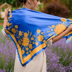 May include: A woman wearing a blue silk scarf with a yellow sunflower pattern and the word "UKRAINE" printed on it. The scarf is tied around her neck and she is standing in a field of lavender.