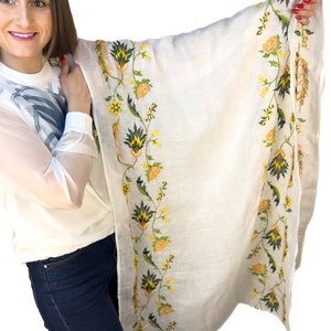 Puede incluir: Una bufanda blanca con un borde floral en tonos amarillos y verdes. La bufanda est&aacute; hecha de una tela ligera y es perfecta para agregar un toque de elegancia a cualquier atuendo.