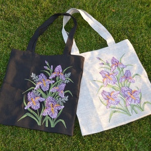 May include: Two tote bags with embroidered purple iris flowers. One bag is black and the other is white.
