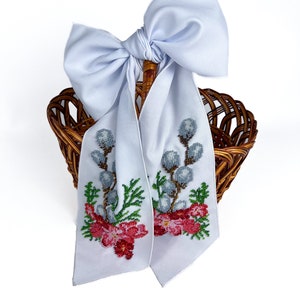 May include: A white wicker basket with a white satin bow and beaded floral embroidery. The embroidery features pink flowers, green leaves, and grey willow branches.