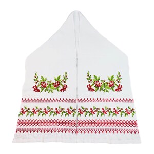 K&ouml;nnte beinhalten: Wei&szlig;es besticktes Textil mit roten Beeren, gr&uuml;nen Bl&auml;ttern und braunen Eicheln. Das Design umfasst einen roten geometrischen Rand. Das Textil ist dreieckig gefaltet, wahrscheinlich ein dekoratives St&uuml;ck.