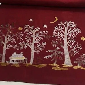 Pode incluir: Caminho de mesa vermelho com uma cena de inverno bordada em fio dourado e prateado. A cena apresenta uma pequena casa, árvores e uma lua crescente.