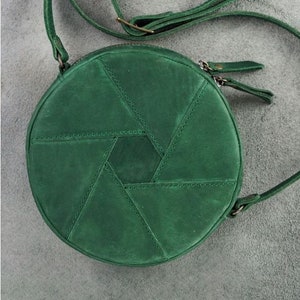Op de afbeelding: Een ronde, groene leren schoudertas met een geometrisch patroon. De tas heeft een lange verstelbare schouderband en een ritssluiting.