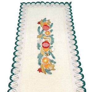 May include: Cream-colored rectangular table runner with a green scalloped border. The center features an embroidered design of oranges, red ornaments, and gingerbread cookies, accented with green sprigs and star shapes.