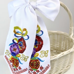 May include: White embroidered Easter egg towels with colourful beaded designs and a white bow. The towels feature red, blue, yellow, and purple egg patterns with gold accents and a red floral border. A white wicker basket is in the background.