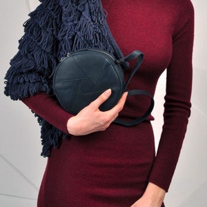Puede incluir: Una mujer lleva un vestido de punto color burdeos con un c&aacute;rdigan de flecos azul marino y un bolso bandolera redondo de cuero azul marino.