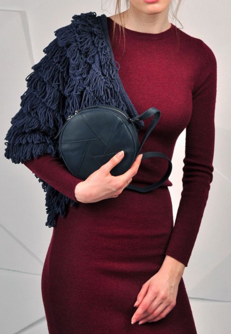 Puede incluir: Una mujer lleva un vestido de punto color burdeos con un c&aacute;rdigan de flecos azul marino y un bolso bandolera redondo de cuero azul marino.