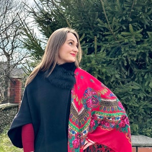 May include: A woman wearing a black coat with a fur collar and a red shawl with floral embroidery. The shawl has fringe trim and is draped over her shoulder.