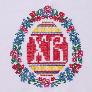 Peut inclure: Un &oelig;uf de P&acirc;ques brod&eacute; en rouge, jaune et bleu avec une couronne de fleurs autour. La couronne est faite de fleurs vertes, bleues, roses et blanches.