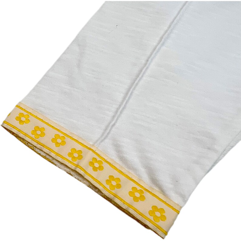 May include: White fabric with a yellow daisy trim. The trim is a band of yellow daisies on a cream background.
