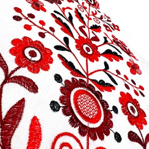 K&ouml;nnte beinhalten: Rote und schwarze Stickerei mit floralem Muster auf wei&szlig;em Stoffhintergrund. Das Design zeigt stilisierte Blumen mit runden Zentren und filigranen Details.