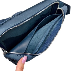 May include: A blue leather zippered pouch with a zippered pocket inside. The pouch is open and the inside is visible.