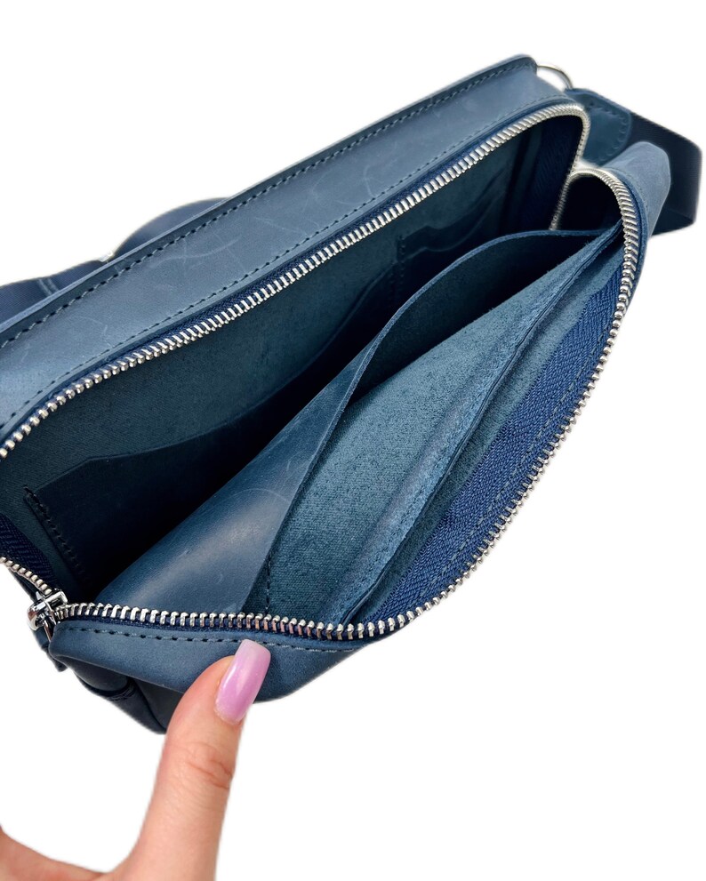 May include: A blue leather zippered pouch with a zippered pocket inside. The pouch is open and the inside is visible.
