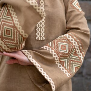 Pu&ograve; includere: Una tunica di lino marrone con motivi geometrici ricamati in tonalit&agrave; di marrone, bianco e verde.