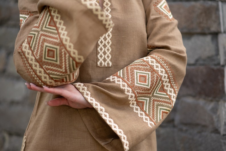 Pu&ograve; includere: Una tunica di lino marrone con motivi geometrici ricamati in tonalit&agrave; di marrone, bianco e verde.