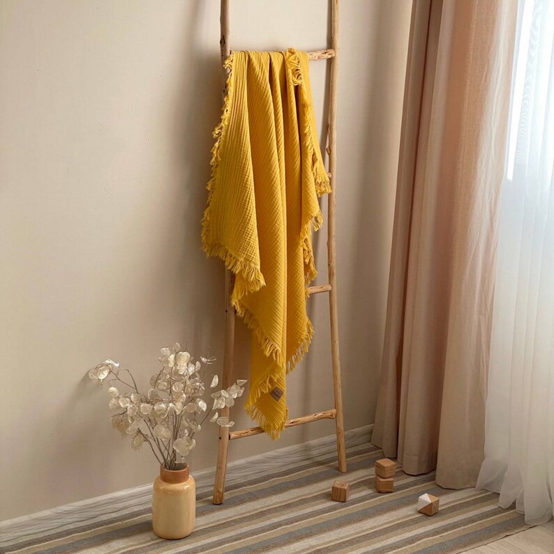 Peut inclure: Une couverture en tissu gaufr&eacute; jaune avec des franges accroch&eacute;e &agrave; une &eacute;chelle en bois. La couverture est pli&eacute;e en deux et drap&eacute;e sur l'&eacute;chelle.