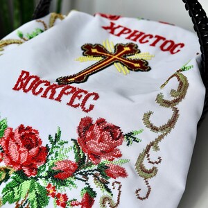 K&ouml;nnte beinhalten: Wei&szlig;es besticktes Tuch mit roten Rosen und gr&uuml;nen Bl&auml;ttern. Das Tuch tr&auml;gt die Worte "Христос Воскрес" in Rot sowie ein Kreuz. Das Tuch liegt in einem schwarzen geflochtenen Korb.