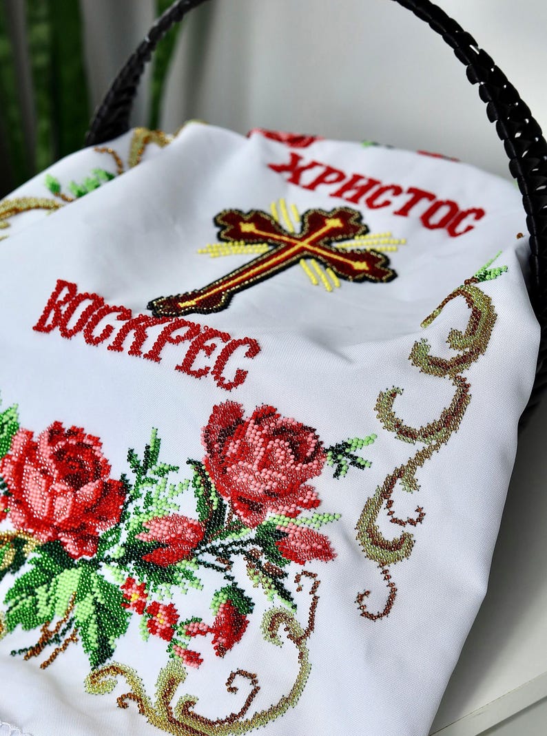 K&ouml;nnte beinhalten: Wei&szlig;es besticktes Tuch mit roten Rosen und gr&uuml;nen Bl&auml;ttern. Das Tuch tr&auml;gt die Worte "Христос Воскрес" in Rot sowie ein Kreuz. Das Tuch liegt in einem schwarzen geflochtenen Korb.