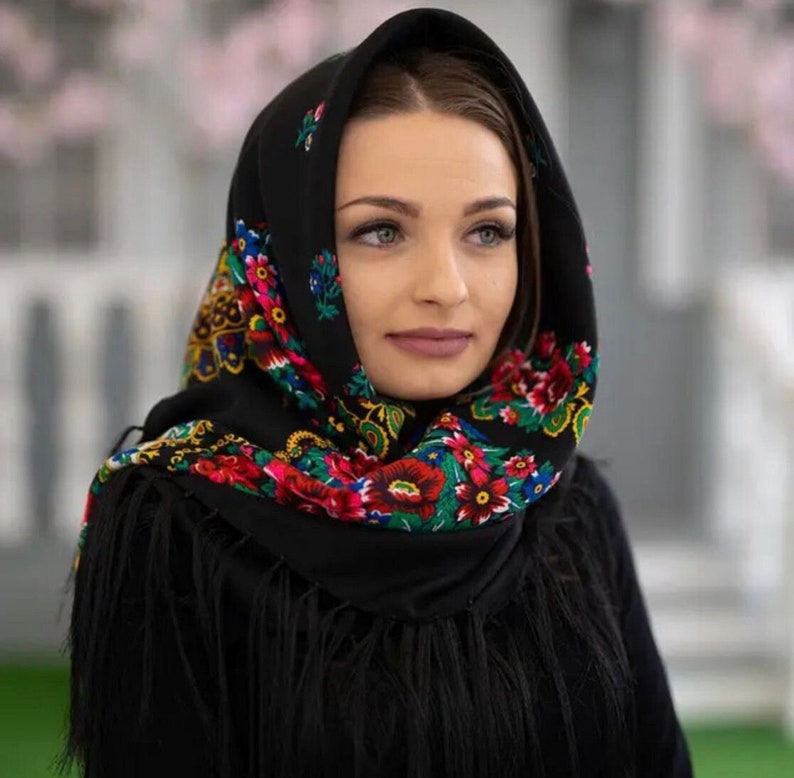 Pu&ograve; includere: Una donna indossa un foulard nero con un motivo floreale colorato. Il foulard ha frange sui bordi.