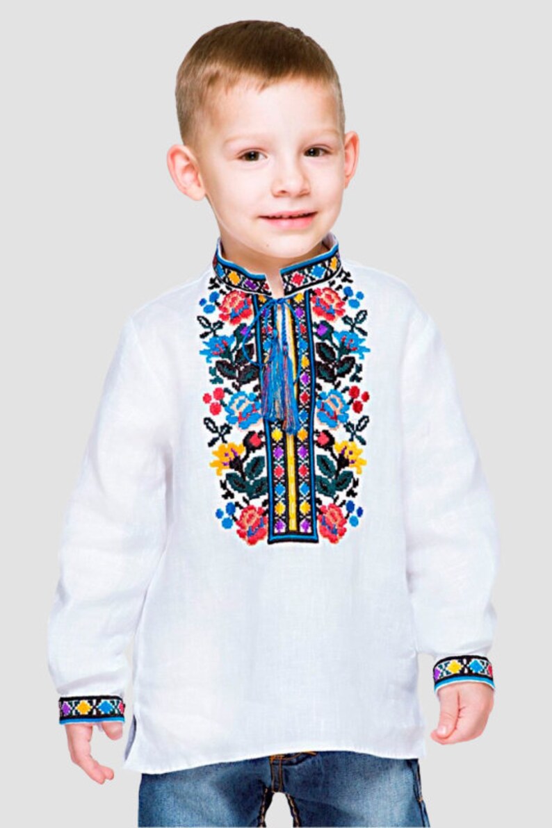 May include: A white long-sleeved shirt with colorful embroidered flowers on the front. The shirt has a blue tassel and a white collar.
